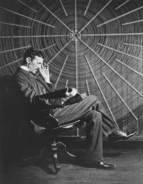 Nikola Tesla, with Rudjer Boscovich's book "Theoria Philosophiae Naturalis", in front of the spiral coil of his high-voltage Tesla coil transformer at his East Houston St., New York, laboratory.