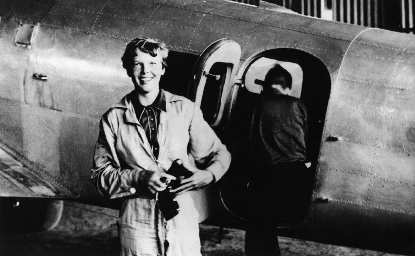 American aviator/pilot Amelia Earhart (1897-1937) standing by her Lockheed Electra dressed in overalls, with Fred Noonan getting into the plane in the background. Parnamerim airfield, Natal, Brazil.