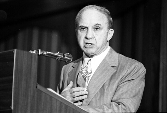 Ex-convict Mickey Cohen during question/answer period of the state-wide Ex-Felon Consortium at the Sheraton Airport Hotel. Credit: Larry Downing, Los Angeles Times - https://digital.library.ucla.edu/catalog/ark:/21198/zz001808b2, CC BY 4.0